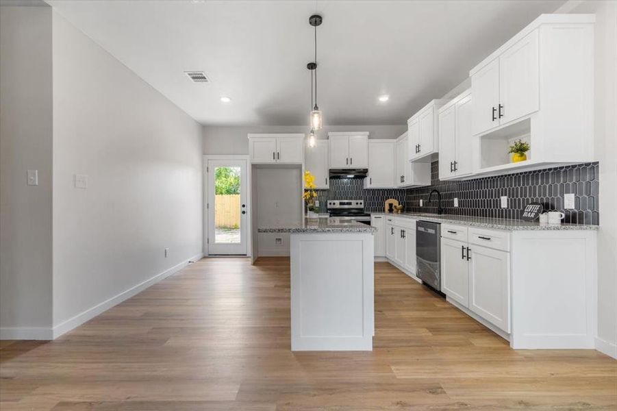 Kitchen with appliances with stainless steel finishes, white cabinetry, tasteful backsplash, and light wood-type flooring