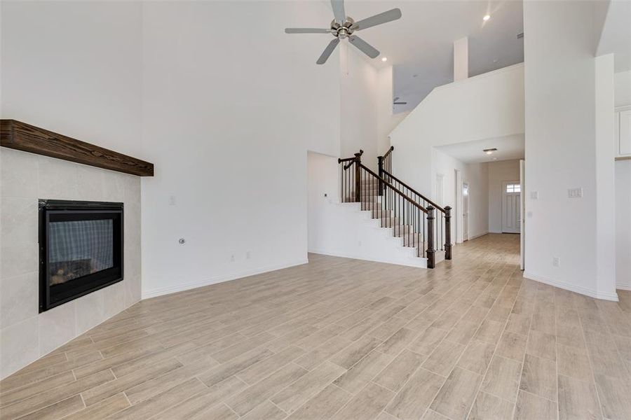 Unfurnished living room with a tile fireplace, a high ceiling, light hardwood / wood-style flooring, and ceiling fan