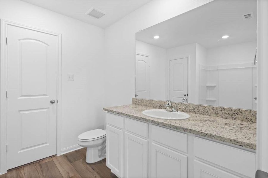 Primary bathroom includes granite counters, designer white cabinetry and luxury vinyl plank flooring.