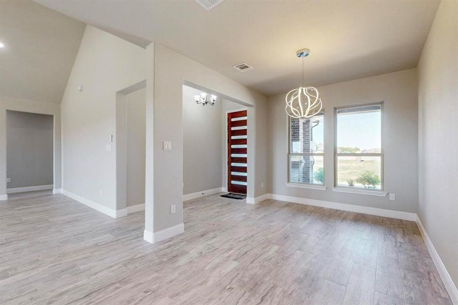 Spare room with vaulted ceiling, light wood-type flooring, and a chandelier