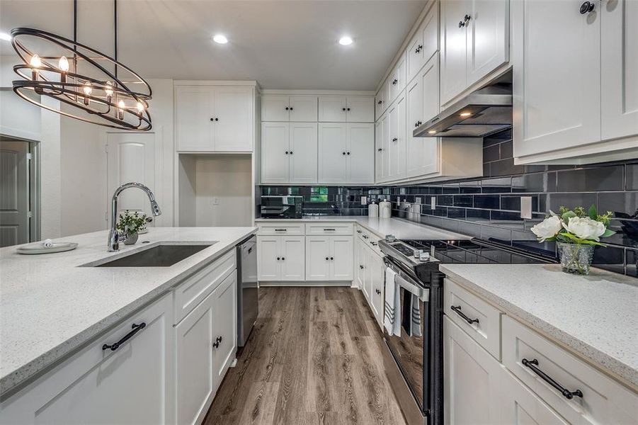 Kitchen with sink, wood-type flooring, light stone countertops, tasteful backsplash, and stainless steel appliances