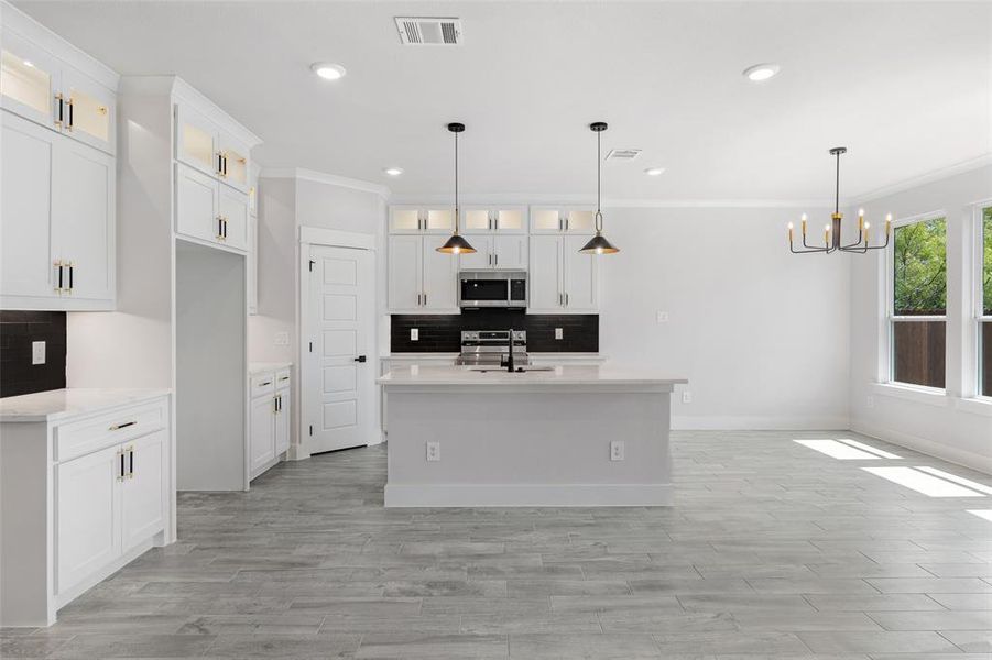 Kitchen featuring decorative light fixtures, an island with sink, white cabinetry, and sink