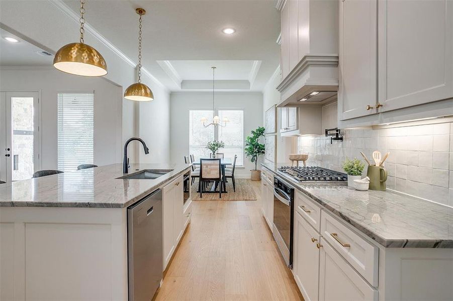 Kitchen with decorative light fixtures, white cabinets, a center island with sink, a raised ceiling, and light hardwood / wood-style floors