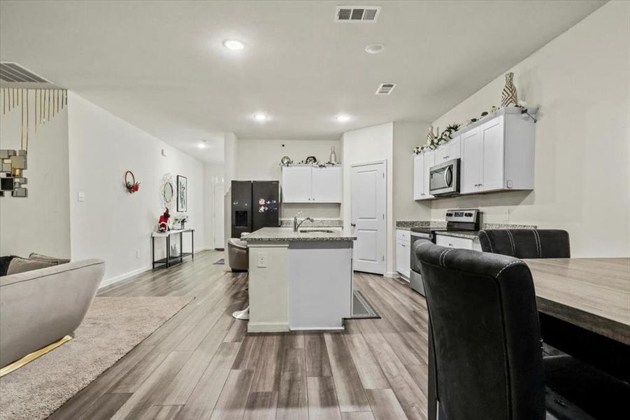 Kitchen with white cabinetry, a kitchen bar, hardwood / wood-style flooring, a center island with sink, and appliances with stainless steel finishes