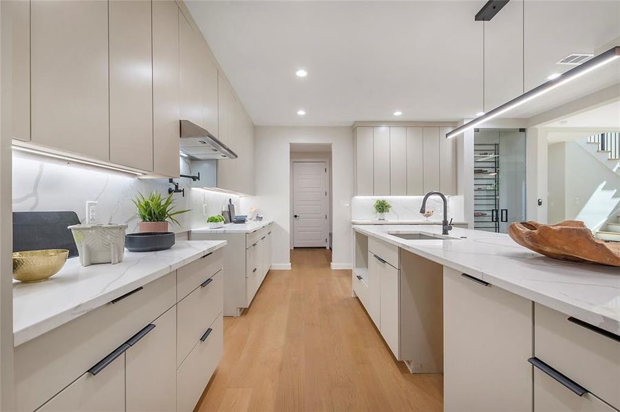 Kitchen with decorative light fixtures, wall chimney range hood, light stone countertops, and light hardwood / wood-style flooring