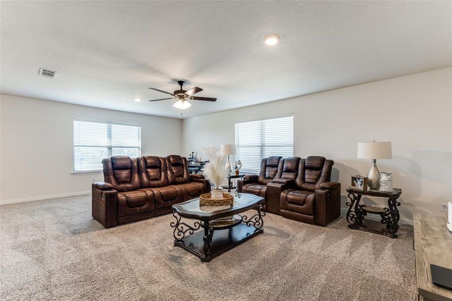 Carpeted living room featuring ceiling fan, plenty of natural light, and a textured ceiling