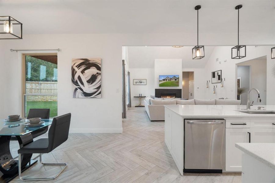 Kitchen with hanging light fixtures, white cabinets, light parquet flooring, dishwasher, and sink