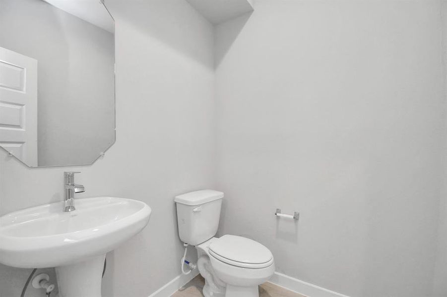 Experience modern elegance in this charming half bathroom, boasting a sophisticated 5-panel door, upgraded pedestal sink, contemporary hardware, and bright recessed lights. Sample photo of completed home. Actual colors and selections may vary.