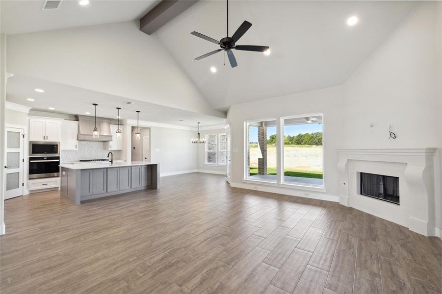 Unfurnished living room featuring dark wood-type flooring, high vaulted ceiling, ceiling fan with notable chandelier, beam ceiling, and sink