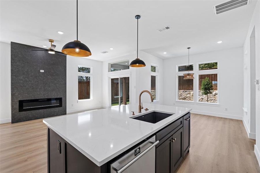 Kitchen featuring an island with sink, a large fireplace, ceiling fan, stainless steel dishwasher, and sink