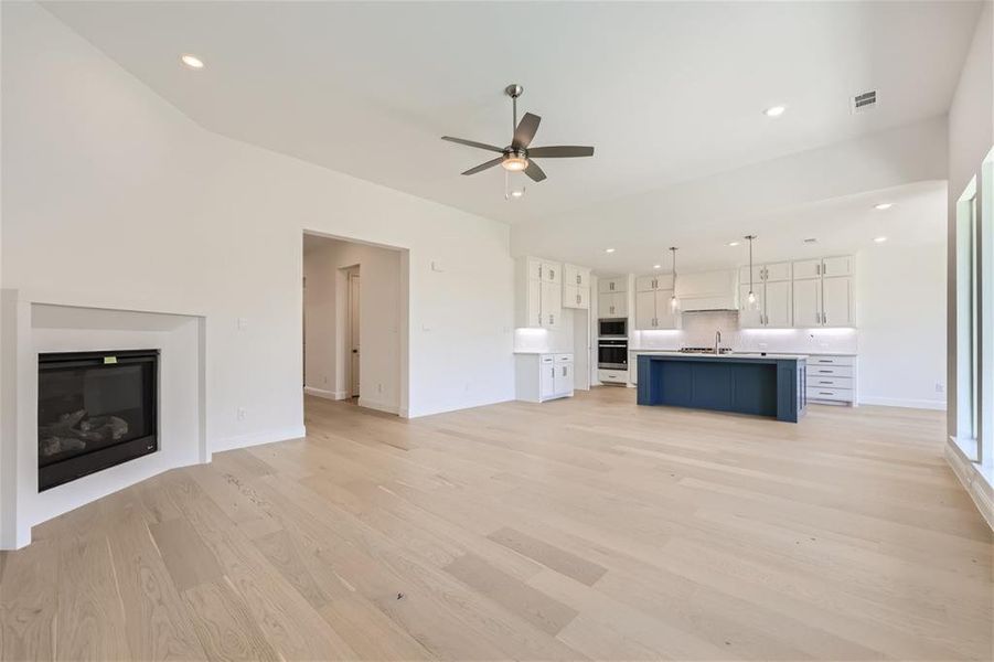 Unfurnished living room featuring sink, ceiling fan, and light wood-type flooring