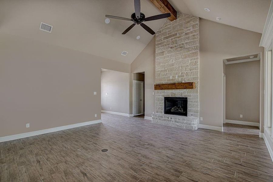 Unfurnished living room with hardwood / wood-style flooring, a fireplace, beam ceiling, high vaulted ceiling, and ceiling fan