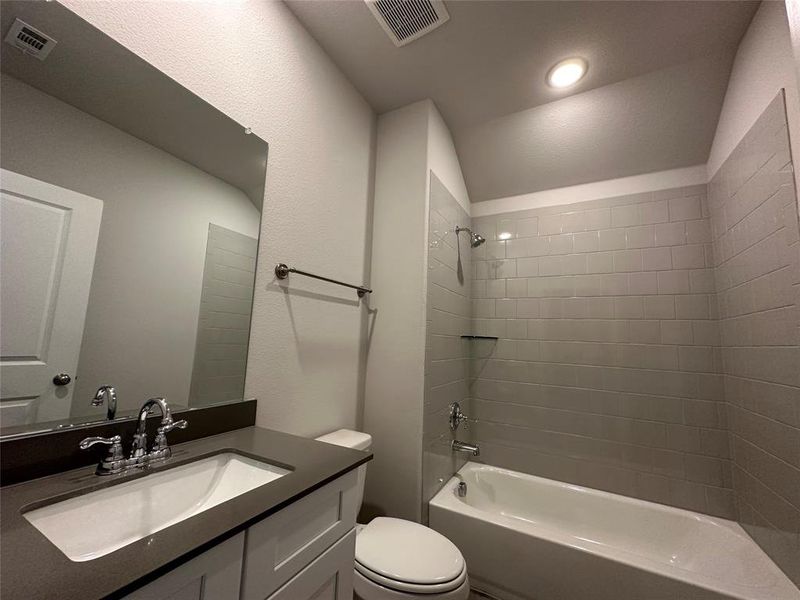 Full bathroom featuring toilet, tiled shower / bath combo, vanity, and vaulted ceiling