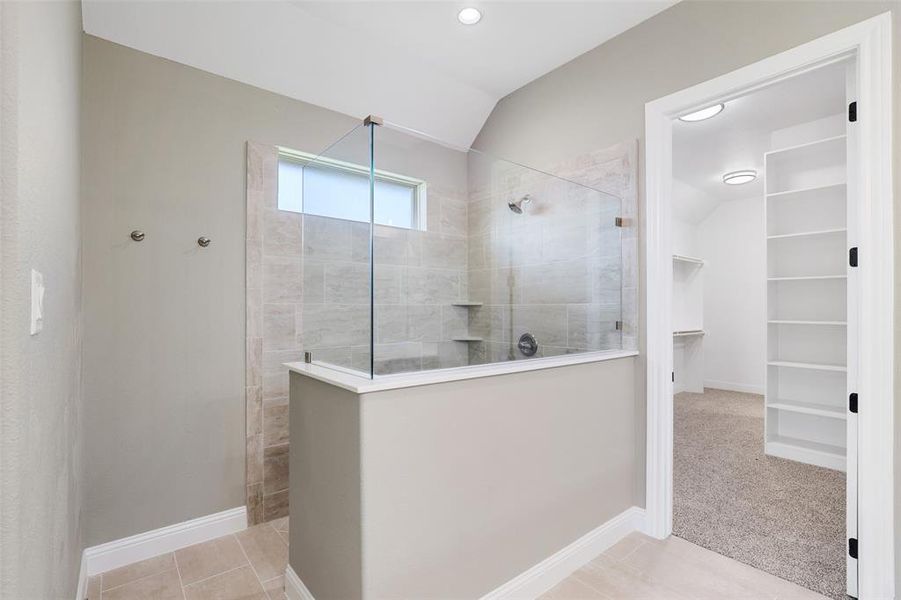 Bathroom featuring a tile shower, tile patterned flooring, and vaulted ceiling