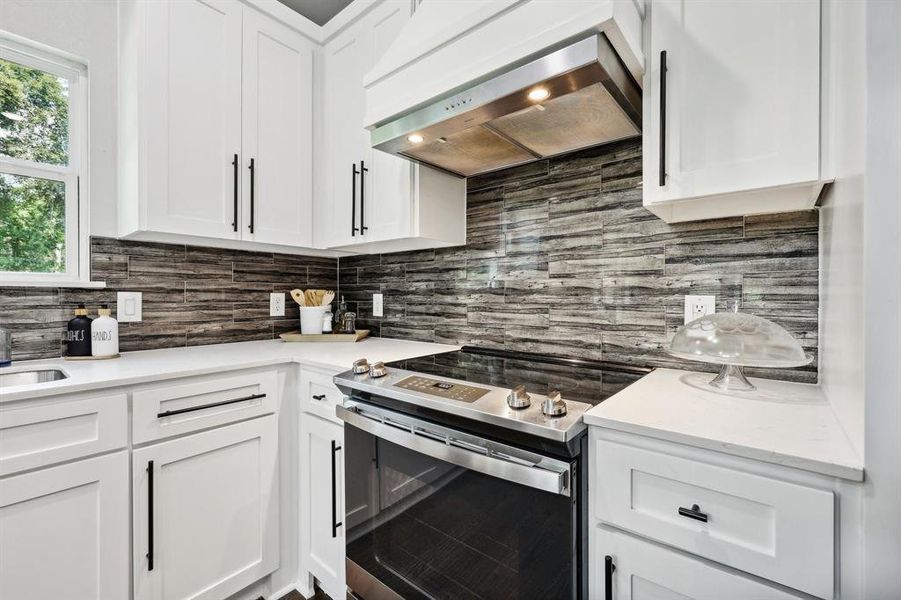 Kitchen with stove, decorative backsplash, white cabinets, and wall chimney exhaust hood