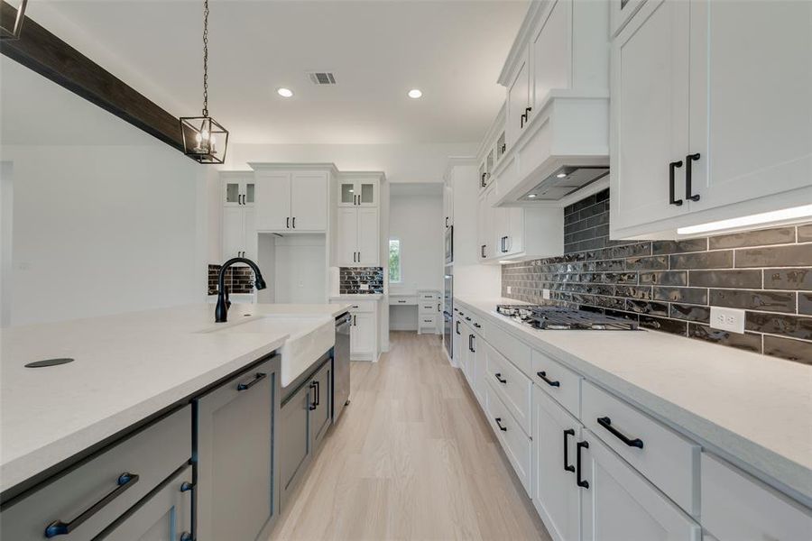 Kitchen with stainless steel appliances, white cabinets, sink, pendant lighting, and backsplash