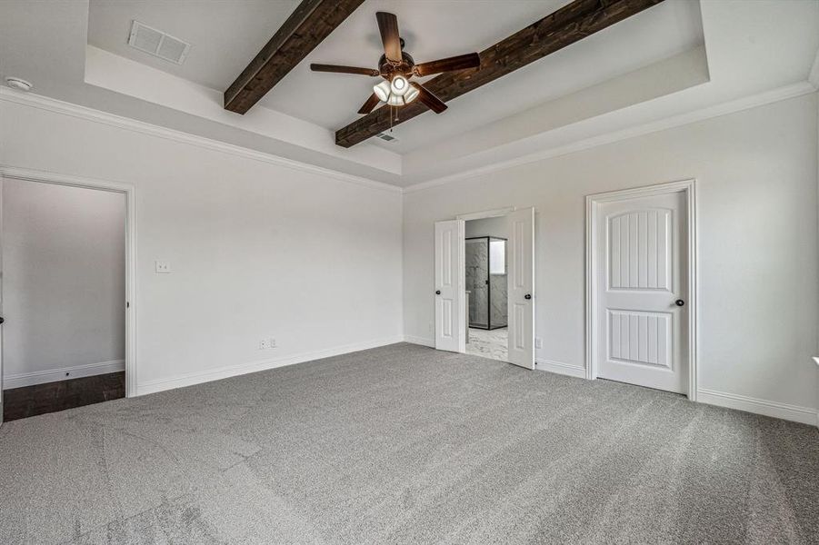 Carpeted spare room featuring crown molding, beamed ceiling, ceiling fan, and a raised ceiling