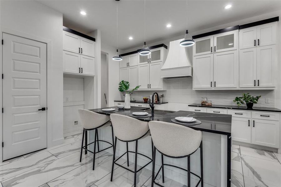 View of large kitchen island and custom cabinetry and hood vent.