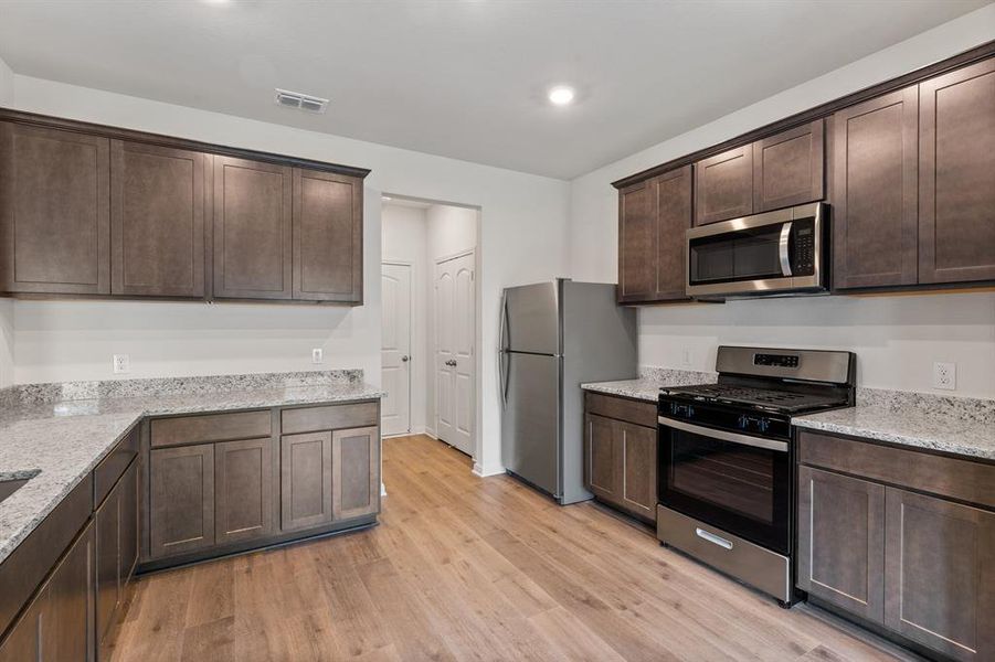 Kitchen featuring dark cabinetry, light stone countertops, light wood-style flooring, and stainless steel appliances