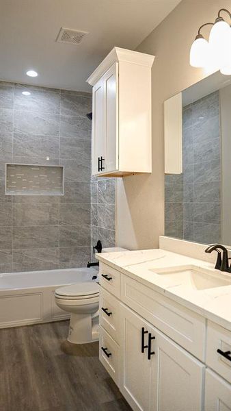 Full bathroom featuring vanity, hardwood / wood-style floors, tiled shower / bath combo, and toilet