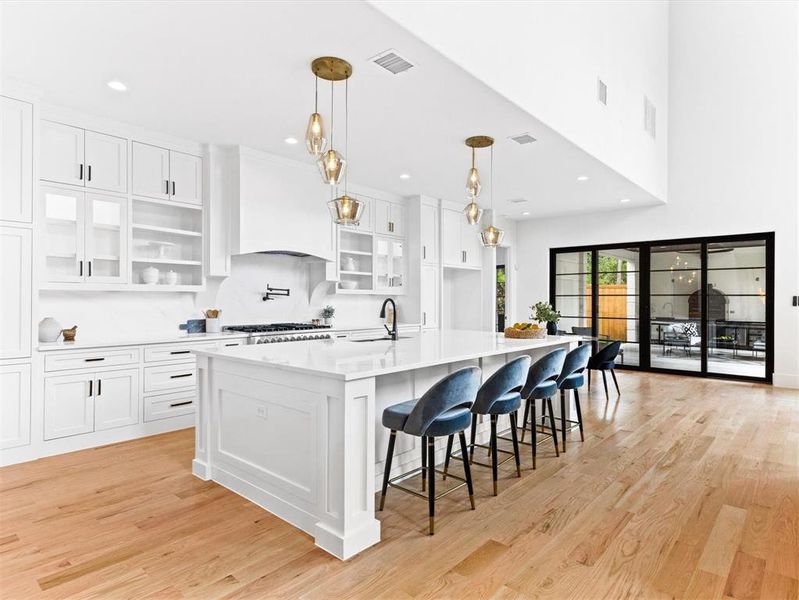 Kitchen featuring light hardwood / wood-style floors, hanging light fixtures, an island with sink, white cabinets, and premium range hood