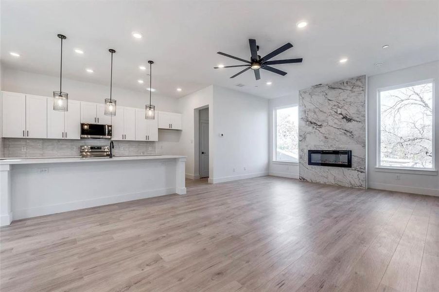 Kitchen with a high end fireplace, pendant lighting, appliances with stainless steel finishes, white cabinetry, and ceiling fan