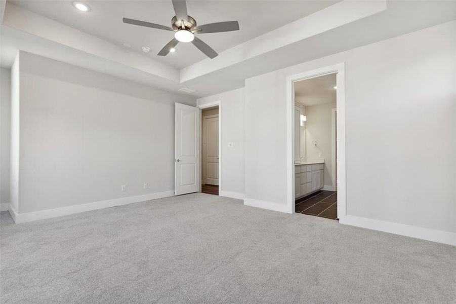 Unfurnished bedroom featuring dark tile flooring, ceiling fan, a raised ceiling, and ensuite bath