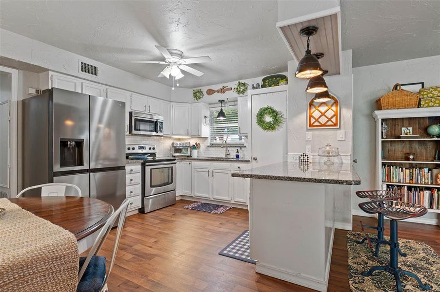 Kitchen with SS appliances with stainless steel finishes, kitchen peninsula, white cabinetry, ceiling fan, and wood-type flooring