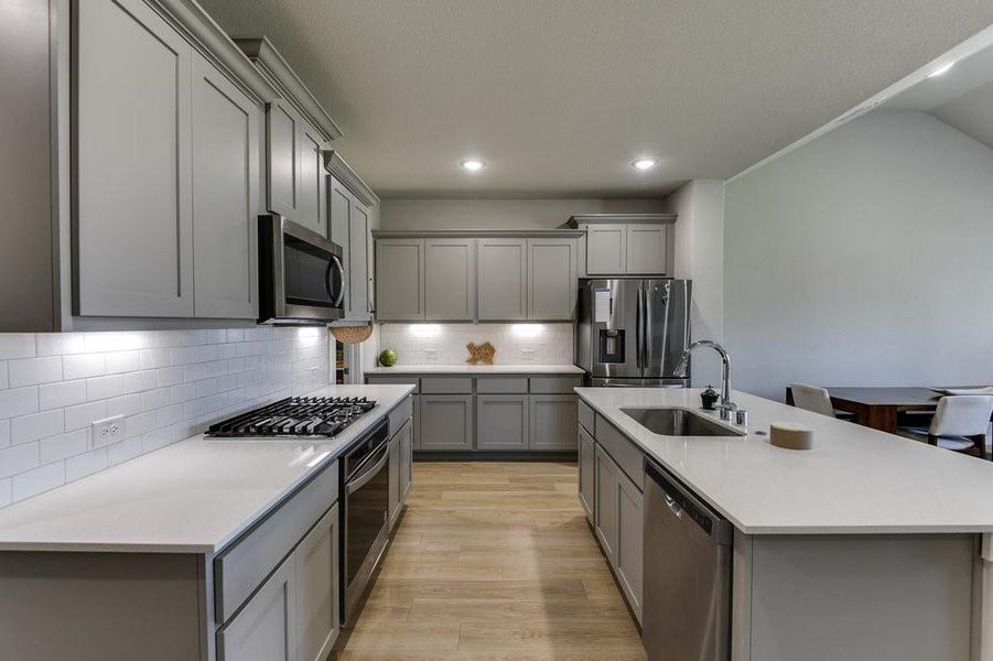 This modern kitchen boasts sleek light gray cabinets, decorative custom backsplash, stainless steel appliances, granite counters  and an island.