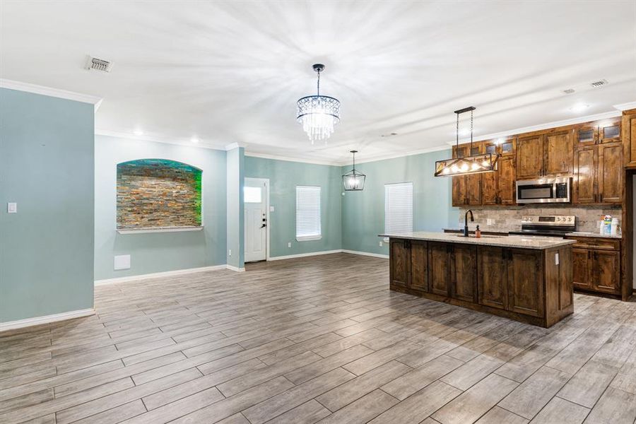 Kitchen with pendant lighting, light hardwood / wood-style floors, appliances with stainless steel finishes, and a kitchen island with sink