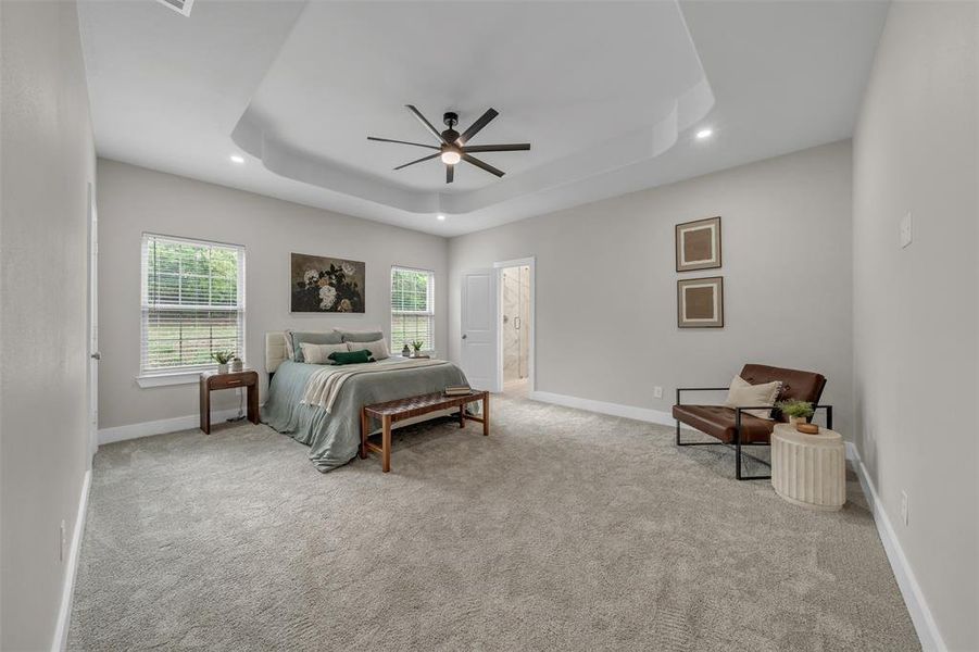 Master bedroom featuring ensuite bathroom, ceiling fan, and a tray ceiling