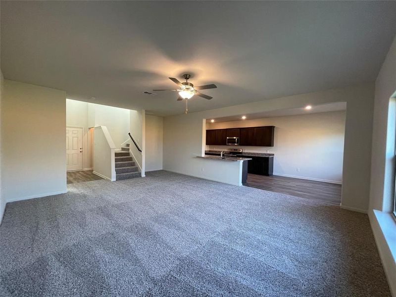 Unfurnished living room with sink, dark colored carpet, and ceiling fan