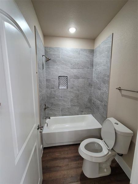 Bathroom with hardwood / wood-style flooring, a textured ceiling, tiled shower / bath combo, and toilet