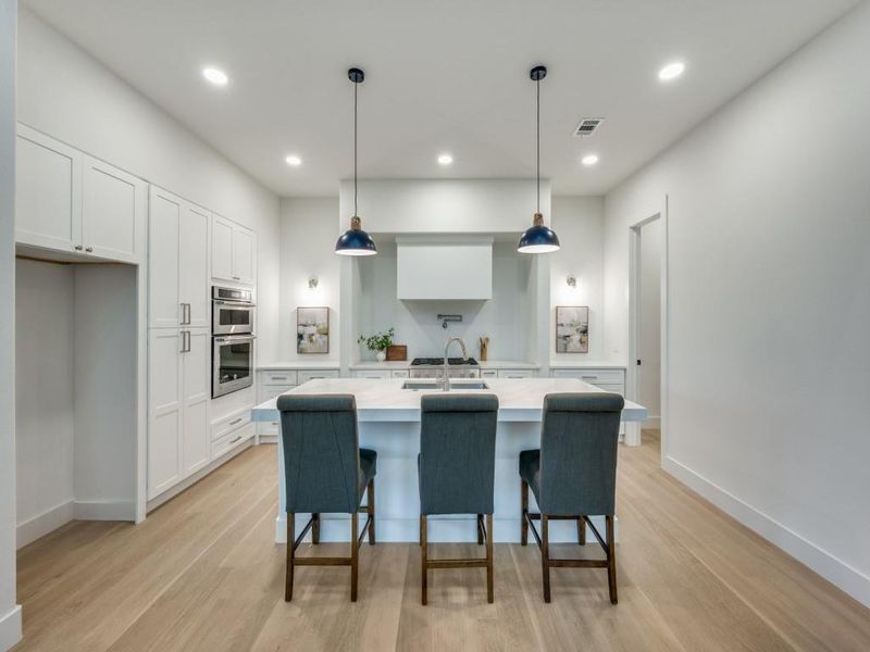 Kitchen featuring a center island with sink, pendant lighting, double oven, white cabinetry, and light wood-type flooring