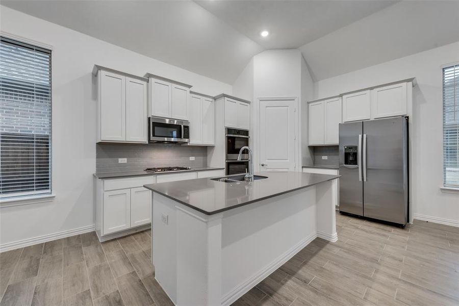 Kitchen with white cabinetry, a center island with sink, light hardwood / wood-style flooring, appliances with stainless steel finishes, and tasteful backsplash