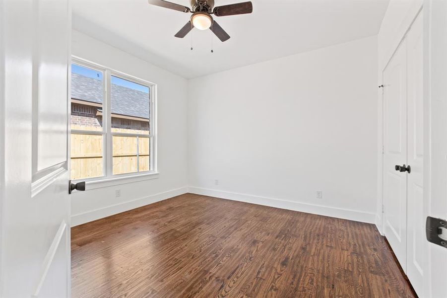 Spare room with dark wood-type flooring, ceiling fan, and a healthy amount of sunlight