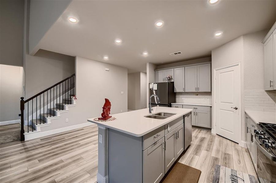 Kitchen featuring a center island with sink, light hardwood / wood-style flooring, tasteful backsplash, and appliances with stainless steel finishes