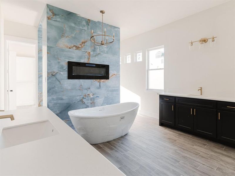 Bathroom featuring a tub, a tiled fireplace, vanity, and a chandelier