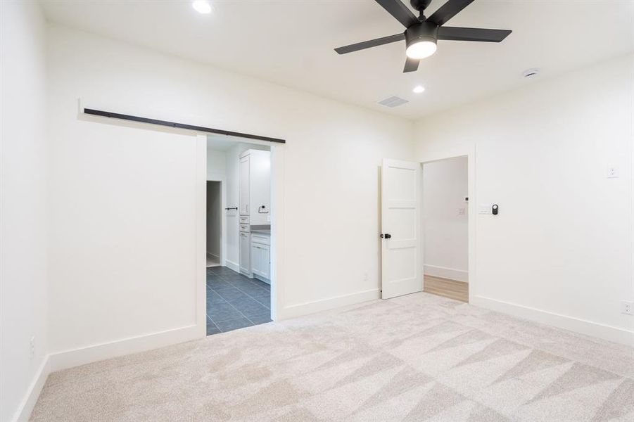 Unfurnished bedroom with connected bathroom, carpet, a barn door, and ceiling fan