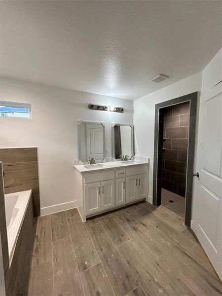 Bathroom featuring vanity, a textured ceiling, plus walk in shower, and wood-type flooring