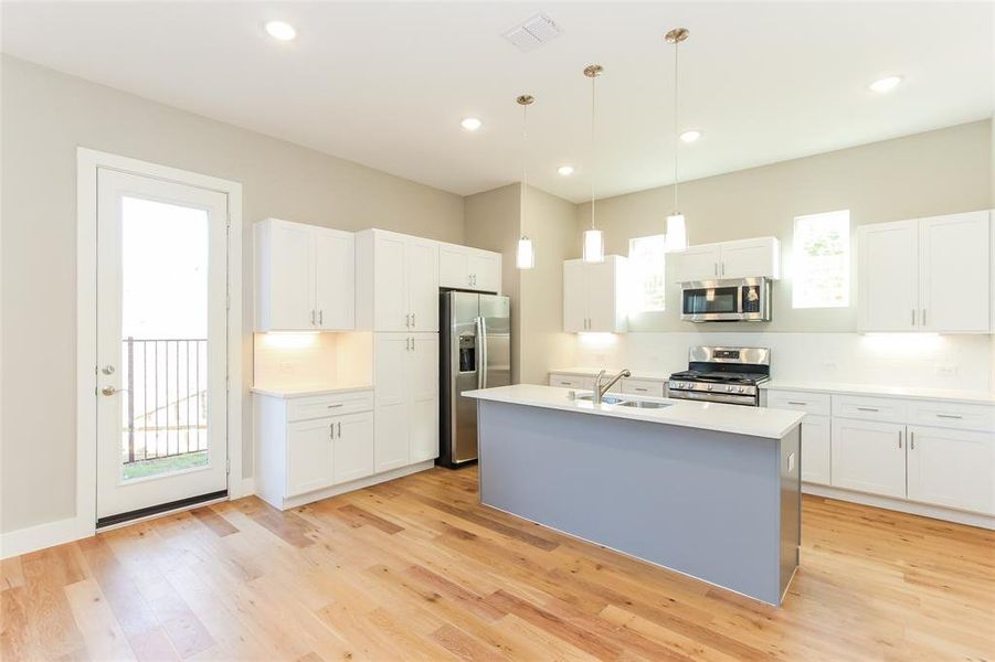 Kitchen with decorative light fixtures, appliances with stainless steel finishes, white cabinets, and a healthy amount of sunlight