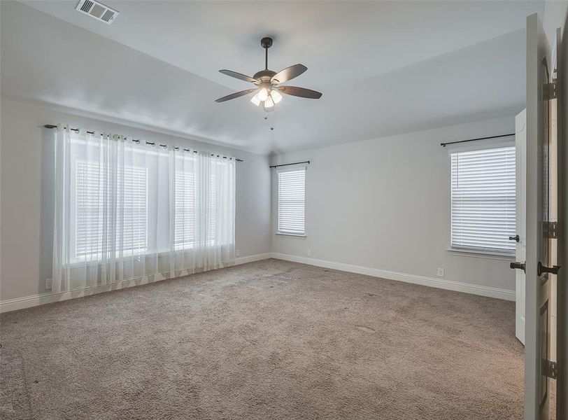 Empty room with a wealth of natural light, carpet floors, and ceiling fan