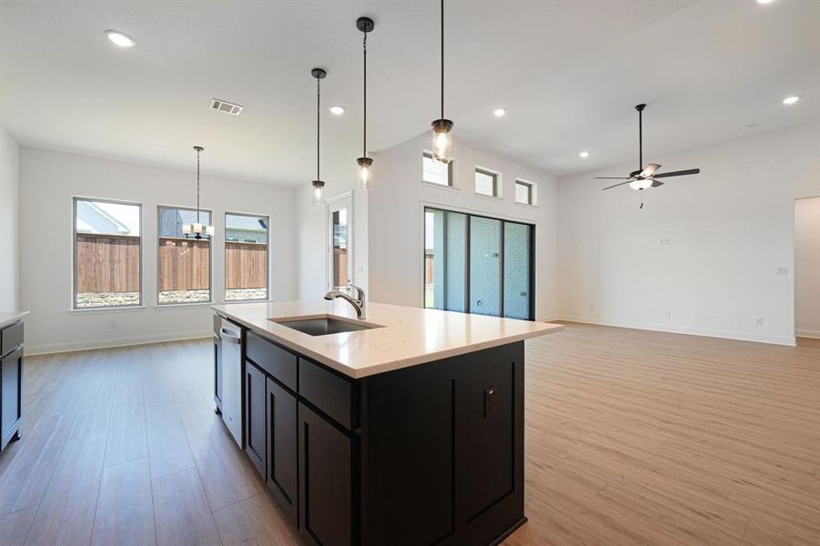 Kitchen featuring hanging light fixtures, light hardwood / wood-style flooring, an island with sink, sink, and dishwasher