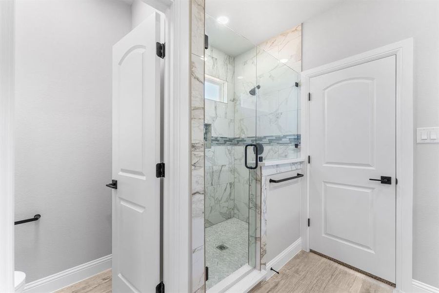 Bathroom with wood-type flooring, a shower with shower door, and toilet