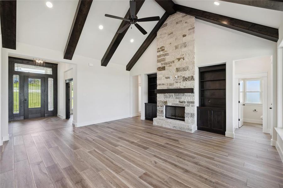 Unfurnished living room with hardwood / wood-style floors, high vaulted ceiling, ceiling fan with notable chandelier, and a stone fireplace