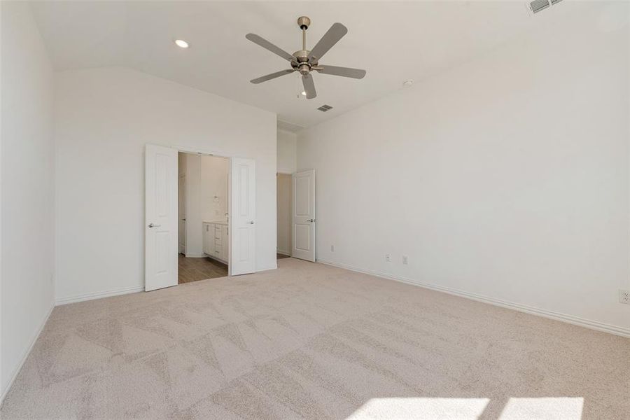 Unfurnished bedroom featuring ceiling fan, light colored carpet, connected bathroom, and vaulted ceiling