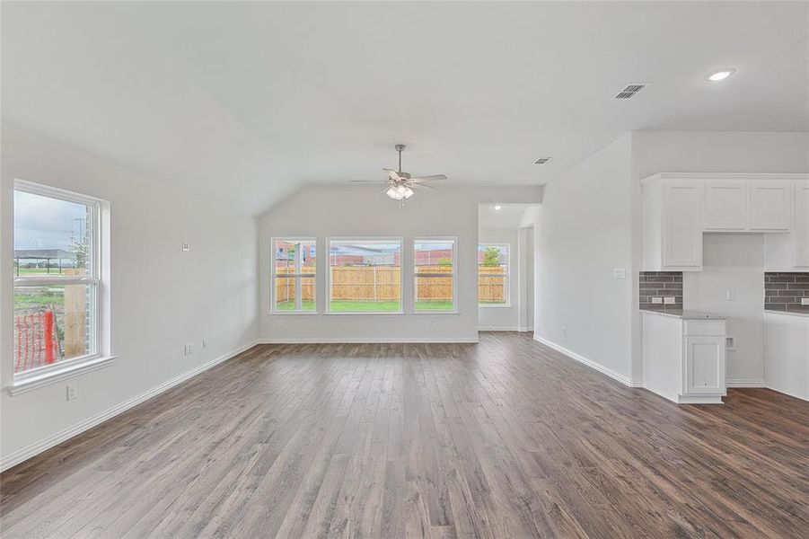 Unfurnished living room with a healthy amount of sunlight, vaulted ceiling, ceiling fan, and hardwood / wood-style flooring