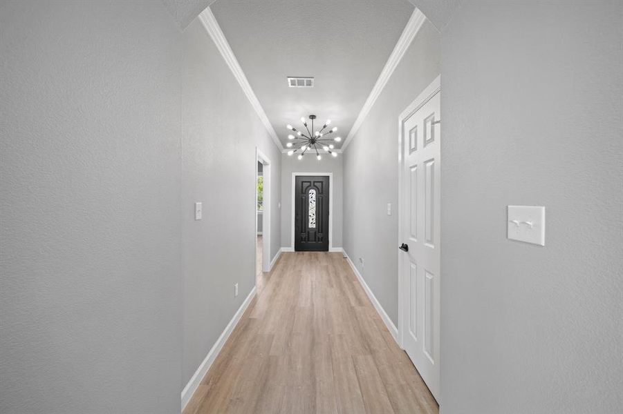 Hallway featuring crown molding, a notable chandelier, and light hardwood / wood-style floors