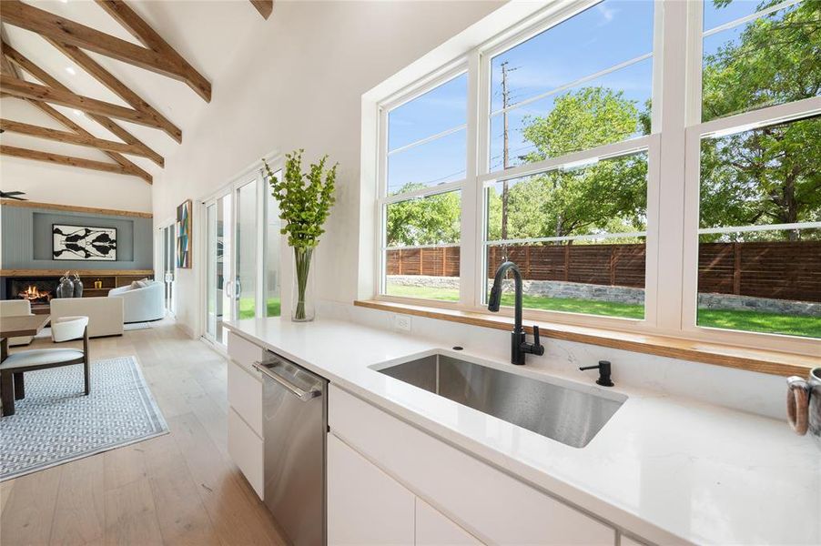 Kitchen with white cabinetry, light wood-type flooring, stainless steel dishwasher, sink, and high vaulted ceiling