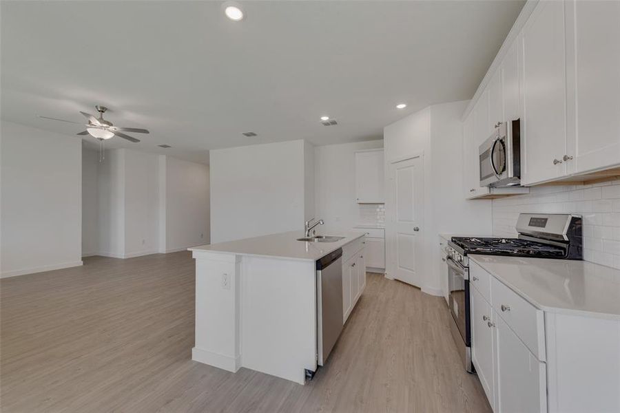 Kitchen with light hardwood / wood-style flooring, an island with sink, stainless steel appliances, ceiling fan, and white cabinets